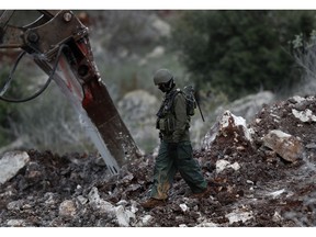 FILE - In this Thursday, Dec. 13, 2018 file photo, an Israeli soldier walks next to an excavator, near the southern border village of Mays al-Jabal, Lebanon, Thursday, Dec. 13, 2018. Lebanon's state-run National News Agency said Monday, 17, 2018 that Lebanese soldiers have gone on alert after Israeli troops placed a barbed wire along the border between the two countries.  The agency said Monday's incident occurred on the edge of the southern village of Mays al-Jabal when Israeli troops laid 200-meters (yards) of wire.