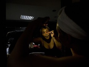 In this Dec. 4, 2018 photo, dancer Morelis Silva uses a cell phone to provide illumination to apply makeup in preparation for the contemporary dance production Ubuntu, at the Teresa Carreno Theater in Caracas, Venezuela.