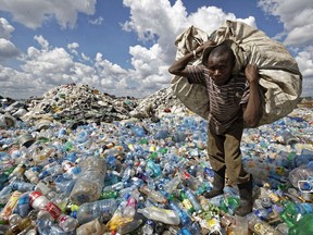 In this photo taken Wednesday, Dec. 5, 2018, a man walks on a mountain of plastic bottles as he carries a sack of them to be sold for recycling after weighing them at the dump in the Dandora slum of Nairobi, Kenya. As the world meets again to tackle the growing threat of climate change, how the continent tackles the growing solid waste produced by its more than 1.2 billion residents, many of them eager consumers in growing economies, is a major question in the fight against climate change.