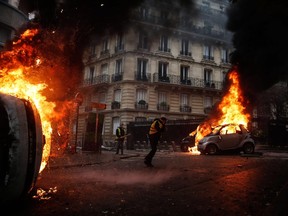 Protesters walk by burning cars during clashes with riot police on the sideline of a protest of Yellow vests (Gilets jaunes) against rising oil prices and living costs, on December 1, 2018 in Paris.