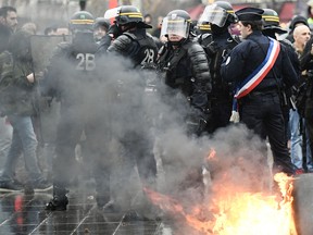 Anti-riot police officers stand guard by a bin set on fire during a demonstration by high school students at place de la Republique in Paris, on December 7, 2018 .