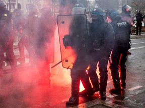 Riot police walk forward past a flare lying on the ground during a protest of "Yellow Vests" on Dec. 8, 2018.