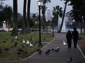 A couple walks under a light rain in the Echo Park in Los Angeles Wednesday, Dec. 5, 2018. A fall storm is causing slick conditions on Southern California freeways but isn't expected to generate enough rain to trigger mudslides or debris flows on hillsides charred by recent fires.