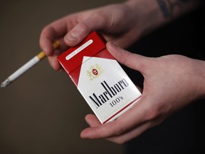 FILE - In this July 17, 2015, file photo, store manager Stephanie Hunt poses for photos with a pack of Marlboro cigarettes, an Altria brand, at a Smoker Friendly shop in Pittsburgh.  Altria is diving into the Canadian cannabis market with a $2.4 billion investment in Toronto-based medical and recreational marijuana provider Cronos Group. The investment from Altria Group Inc.,  would give it about 45 percent ownership of Cronos. Altria will also pay another $1.4 billion for warrants of Cronos Group that if exercised, would give the Altria a 55 percent majority ownership of Cronos.