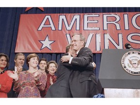 FILE - In this Nov. 8, 1988 file photo, President-elect George H. W. Bush, right, hugs his son George W. Bush, center left, during his victory rally, in Houston, Texas. Other Bush family members are from left: Columba Bush, Jeb Bush, and Laura Bush.  Presidents George H.W. Bush and George W. Bush were both conservatives, but during very different times. The elder Bush was a Republican who could carve an occasional moderate path without a crushing response from the right. His was an era of stepping back from the prospect of doomsday, with the collapse of the Soviet Union, and a far more limited threat emerging with Iraq's invasion of Kuwait. But that was not at all like the Sept. 11 terrorist attacks that came early to his son.