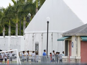 FILE - In this Wednesday, June 20, 2018 file photo, immigrant children walk in a line outside the Homestead Temporary Shelter for Unaccompanied Children, a former Job Corps site that now houses them, in Homestead, Fla. Nearly every adult working with children in the U.S. _ from nannies to teachers to coaches _ has undergone state screenings to ensure they have no proven history of abusing or neglecting kids. One exception: thousands of workers at this and another federal detention facility holding 3,600 migrant teens in the government's care, The Associated Press has learned.