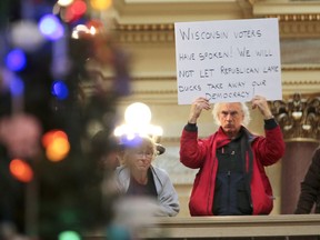 Bob Kinosian, from Wauwatosa, Wis., holds up a sign during the state Christmas Tree lighting ceremony in state Capitol Rotunda Tuesday Dec. 4, 2018, in Madison, Wis. The Senate and Assembly are set to send dozens of changes in state law to Gov. Scott Walker's desk. (Steve Apps