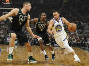 Golden State Warriors' Stephen Curry drives past Milwaukee Bucks' Eric Bledsoe and Brook Lopez during the first half of an NBA basketball game Friday, Dec. 7, 2018, in Milwaukee.