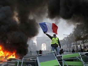 FILE - In this Nov. 24, 2018 file photo, a demonstrator waves the French flag on a burning barricade on the Champs-Elysees avenue with the Arc de Triomphe in background, during a demonstration against the rise of fuel taxes. There are parallels for unpopular French President Emmanuel Macron in the demise of King Louis XVI more than two centuries ago. Democracy has replaced monarchy but the culture of a mob taking its anger against perceived inequality onto the streets of Paris has not changed.