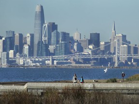 Birdwatchers wear jackets at the Elsie Roemer Bird Sanctuary on Wednesday, Jan. 2, 2019, in Alameda, Calif. San Francisco skyline is seen in background.  Snow is falling on cacti in southern Arizona, while Anchorage is seeing balmy weather - at least by Alaska standards. The weather appears to be flipped throughout much of the West.