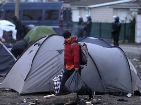 In this photo taken Wednesday, Jan.16, 2019, a migrant carries bags in a makeshift camp as police dismantle the camp in Calais, northern France. Land, sea and air patrols are combing the beaches, dunes and frigid, murky coastal waters of northern France in a bid to end an unusual high-risk tactic by migrants, mostly Iranians: trying to sneak across the English Channel in rubber rafts.