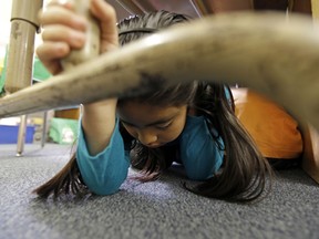 FILE - In this Oct. 17, 2013 file photo, Lillian Zurita shows the proper way to "drop, cover and hold on" in Ms. Irvin's second-grade class during an earthquake drill known as the Great Shakeout at Rosemont Elementary School near downtown Los Angeles. Twenty-five years ago this week, on Jan. 17, 1994, a violent, pre-dawn earthquake shook Los Angeles from its sleep, and sunrise revealed widespread devastation, with dozens killed and $25 billion in damage.