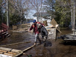 Kevin Gaddess, right, helps a friend navigate over debris from homes and cottages as floodwater continues to flood Route 690 in Princess Park, N.B. on May 12, 2018. A coast-to-coast study finds Canadian homeowners aren't keeping up with the need to protect their houses against catastrophic events made more common by climate change. The study from the University of Waterloo points out that insurance claims from such weather-driven problems like floods have more than quadrupled over the last decade -- even after taking rising real estate prices into account.