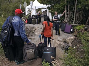 A Royal Canadian Mounted Police officer informs a migrant couple of the location of a legal border station, shortly before they illegally crossed from Champlain, N.Y., to Saint-Bernard-de-Lacolle, Quebec, using Roxham Road on August 7, 2017. Canada's border protection agency has charged a woman in connection with organizing illegal entries into Canada through a popular rural crossing in southern Quebec. A charge was laid against Olayinka Celestina Opaleye Wednesday at the courthouse in Saint-Jean-sur-Richelieu, south of Montreal.