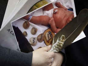 A woman holds a photo of a baby and an eagle feather at a press conference in support of the mother who's newborn baby was seized from hospital by Manitoba's Child and Family Services (CFS) at First Nations Family Advocate Office in Winnipeg on January 11, 2019. Manitoba's First Nations family advocate says a mother who had her newborn baby apprehended will learn this week about when the child will be reunited with family. Social media videos of the two-day-old baby girl being taken away from the arms of her crying mother in a Winnipeg hospital led to outcry online and calls for change from Indigenous leaders.