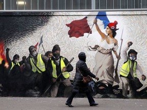 A woman passes by a mural by street artist PBOY depicting Yellow Vest (gilets jaunes) protestors inspired by a painting by Eugene Delacroix, "La Liberte guidant le Peuple" (Liberty Leading the People), in Paris, Thursday, Jan. 10, 2019. French President Emmanuel Macron is facing a mountain of challenges in the new year starting with yellow vest protesters who are back in the streets to show their anger against high taxes and his pro-business policies that they see as favoring the wealthy rather than the working class.