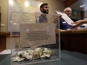 A donation box sits on the counter as Dany Garcia speaks with visitors at the Ernest F. Coe Visitor Center in Everglades National Park, Friday, Jan. 4, 2019, in Homestead, Fla. Garcia is being paid by the Florida National Parks Association to work in the center during the partial government shutdown. As the shutdown drags on, private organizations, local businesses, volunteers and state governments are putting up the money and manpower to keep national parks across the U.S. open, safe and clean for visitors.