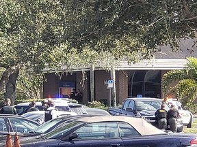 Law enforcement officials take cover outside a SunTrust Bank branch, Wednesday, Jan. 23, 2019, in Sebring, Fla. Authorities say they've arrested a man who fired shots inside the Florida bank. (The News Sun via AP)