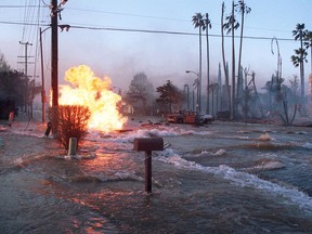 FILE - In this Jan. 17, 1994 file photo, gas from a ruptured supply line burns as water from a broken water main floods Balboa Boulevard in the Granada Hills area of Los Angeles. The fire from the gas main destroyed two homes, right. Twenty-five years ago this week, the violent, pre-dawn earthquake shook Los Angeles from its sleep, and sunrise revealed widespread devastation, with dozens killed and $25 billion in damage.