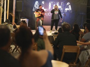 In this Jan. 12, 2019 photo, Venezuelan singer Reymar Perdomo performs with fellow Venezuelan and guitarist Omar Rumbos at a fair on the beach of San Bartolo, Peru. A year ago, Perdomo was singing for spare change on jammed buses, struggling to make ends meet while building a new life in Peru's capital.