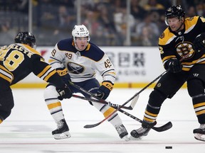 Buffalo Sabres' C.J. Smith (49) battles Boston Bruins' Matt Grzelcyk (48) and David Backes (42) for the puck during the first period of an NHL hockey game in Boston, Saturday, Jan. 5, 2019.