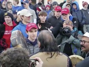 In this Friday, Jan. 18, 2019 image made from video provided by the Survival Media Agency, a teenager wearing a "Make America Great Again" hat, center left, stands in front of an elderly Native American singing and playing a drum in Washington.