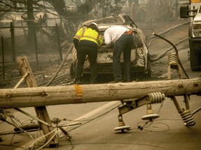 FILE - In this Nov. 10, 2018 file photo, with a downed power utility pole in the foreground, Eric England, right, searches through a friend's vehicle after the wildfire burned through Paradise, Calif. Facing potentially colossal liabilities over deadly California wildfires, PG&E will file for bankruptcy protection. The announcement Monday, Jan. 14, 2019, follows the resignation of the power company's chief executive.