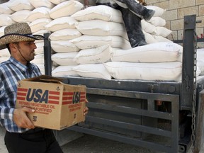 FILE - In this June 4, 2008 file photo, a Palestinian carries a box of vegetable oil as he walks past bags of flour, both donated by the United States Agency for International Development, at a depot in the West Bank village of Anin near Jenin. Tens of thousands of Palestinians are no longer getting food aid or health services from America after the Trump administration's decision in 2018 to cut more than $200 million in aid to the Palestinians. Before the aid cuts were announced, it provided food aid -- branded as a gift from the American people -- to more than 180,000 Palestinians in the Israeli-occupied West Bank and Gaza on behalf of the World Food Program.