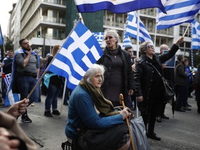 A woman sits down as others hold Greek flags during a rally in Athens, Sunday, Jan. 20, 2019. Greece's Parliament is to vote this coming week on whether to ratify the agreement that will rename its northern neighbor North Macedonia. Macedonia has already ratified the deal, which, polls show, is opposed by a majority of Greeks.