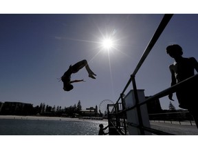 In this Jan. 24, 2019, photo, a beachgoer jumps off a jetty at Glenelg Beach in Adelaide, Australia, as temperatures climb to 45 Celsius (113 ‎Fahrenheit). Australia has sweltered through its hottest month on record in January and the summer of extremes continues with wildfires razing the drought-parched south while expanses of the tropical north are flooded.