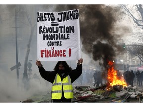 A yellow vest demonstrator holds up a banner reading 'Yellow vest, World Revolution against Finance', as they set up barricades and light fires in Paris, Saturday, Jan. 26, 2019. France's yellow vest protesters hit the streets again Saturday, keeping up pressure on President Emmanuel Macron even as internal divisions and frustration over protest violence cloud the movement's future.