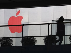 In this Dec. 6, 2018, photo, a woman runs past a Apple logo colored red in Beijing, China. Apple Inc.'s $1,000 iPhone is a tough sell to Chinese consumers who are jittery over an economic slump and a trade war with Washington. The tech giant became the latest global company to collide with Chinese consumer anxiety when CEO Tim Cook said iPhone demand is waning, due mostly to China. Weak consumer demand in the world's second-largest economy is a blow to industries from autos to designer clothing that are counting on China to drive revenue growth.