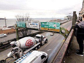 In this photo taken Wednesday, Jan. 2, 2019, a woman takes a photo toward Elliott Bay as Alaskan Way Viaduct traffic rolls past her below ahead of an upcoming closure of the roadway, in Seattle. The double-decker highway along Seattle's waterfront is set to shut down for good Friday, Jan. 11, ushering in what officials say will be one of the most painful traffic periods in the city's history. The 65-year-old viaduct is being replaced by a four-lane Highway 99 tunnel, scheduled to open several weeks after the viaduct's closure.