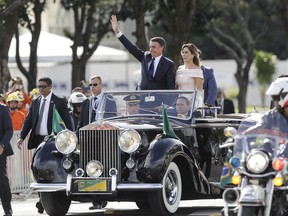 Flanked by first lady Michelle Bolsonaro, Brazil's President Jair Bolsonaro waves as he rides in an open car after his swearing-in ceremony, in Brasilia, Brazil, Tuesday, Jan. 1, 2019.