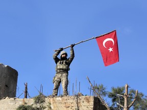 FILE -- In this Sunday, Jan. 28, 2018 file photo, a soldier waves a Turkish flag as Turkish troops secure Bursayah hill, which separates the Kurdish-held enclave of Afrin from the Turkey-controlled town of Azaz, Syria. The planned U.S. troop withdrawal opens a void in the north and east of Syria, and the conflicts and rivalries among all the powers in the Middle East are converging to fill it.