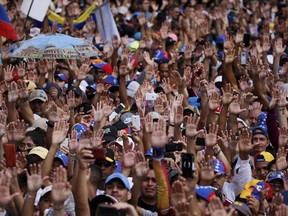 Anti-government protesters hold their hands up during the symbolic swearing-in of Juan Guaido, head of the opposition-run congress, who declared himself interim president of Venezuela, during a rally demanding President Nicolas Maduro's resignation in Caracas, Venezuela, Wednesday, Jan. 23, 2019.