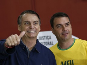 FILE - In this Oct. 7, 2018 file photo, then-presidential frontrunner Jair Bolsonaro, left, accompanied by his son Flavio Bolsonaro, arrives to vote in the general election in Rio de Janeiro, Brazil. Flavio, the son of current President Jair Bolsonaro, is fending off suspicions of financial irregularities that are starting to cast a shadow over the new administration.