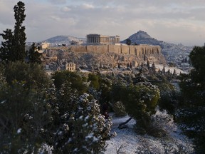 A man walks at Filopappos hill as at the background is seen the ancient Acropolis hill with the 500BC Parthenon temple, after a snowfall in Athens , on Tuesday, Jan. 8, 2019.