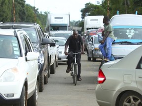 A cyclist makes his way through a fuel queue in the capital Harare, Friday, Jan. 11, 2019. Zimbabwe's president has more than doubled the price of gasoline, hoping the increase will end severe shortages that are fueling public anger.