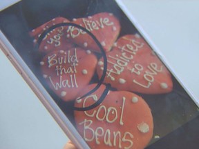 In this Jan. 24, 2019, video image provided by KING-TV, Ana Carrera shows her phone with a photo of cookies she posted in Facebook, after she took the picture at Edmonds Bakery in Edmonds, Wash. Ken Bellingham, who owns the bakery, is apologizing for a politically charged Valentine's Day cookie that generated an uproar on social media. KING-TV reports that Bellingham has gotten phone calls from frustrated customers about the heart-shaped cookie with "Build that Wall" in frosting letters.