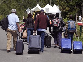 A family from Haiti approaches an RCMP tent on the border in St. Bernard-de-Lacolle, Que., as they haul their luggage down Roxham Road in Champlain, N.Y., to enter Canada illegally on Aug. 7, 2017.