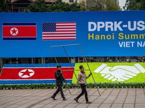 Workers carry a frame past a display board announcing the forthcoming DPRK-USA summit, at the international media centre on February 24, 2019 in Hanoi, Vietnam.