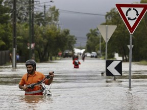 In this Sunday, Feb. 3, 2019, photo, a resident pushes a bicycle through floodwaters at Hermit Park in Townsville, Australia. Emergency workers are using boats and helicopters to rescue people from flooded parts of northern Australia where forecasts call for more heavy rainfall. More than 1,100 people had been rescued from their homes on Sunday night and evacuation efforts were continuing Monday.