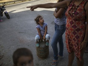 A girl sitting on a full gas container waits for her family to gather before they walk home after buying cooking gas in the Petare slum of Caracas, Venezuela, Sunday, Feb. 10, 2019. Residents pay 3 U.S. cents for each container of natural gas, which is subsidized by the government.