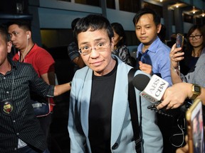 Philippine journalist Maria Ressa  is surrounded by the press as she is escorted by a National Bureau Investigation (NBI) agent  at the NBI headquarters after her arrest in Manila on Feb. 13, 2019.