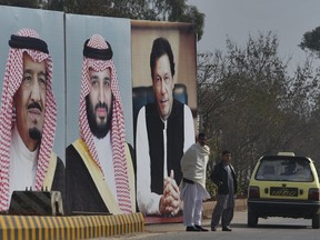 A man with his son waits for transport next to huge portraits of Saudi leaders and a Pakistani prime minister displayed on a highway on the occasion of the visit by Saudi Arabia's crown prince to Pakistan, in Islamabad, Pakistan, Sunday, Feb. 17, 2019. Saudi Crown Prince Mohammed bin Salman will arrive in Islamabad on Sunday evening on an official visit that is expected to include the signing of agreements for billions of dollars of investment in Pakistan.