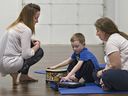 Yoga instructor Trish Leblanc watches as seven-year-old Bennett Cochrane, sitting with his mother Renee, communicates using a tablet on Wednesday, May 20, 2015.