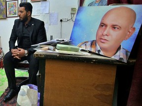 In this photo taken on Tuesday, Feb. 5, 2019, a friend of Alaa Mashzoub, seen in the poster, sits in his room at his home in Karbala, Iraq. Alaa Mashzoub, the Iraqi novelist who was gunned down this week in Karbala, was a secular civil society activist who used his bike to get around the Shiite holy city's infamous traffic and road closures. He was also an outspoken critic of foreign interferences in Iraqi affairs Iraq and political meddling by powerful militias backed by Iran. On Saturday, he was gunned down by unknown assailants who silenced him with 13 bullets as he rode his bicycle home for the last time.