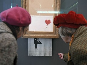 People look at the shredded Banksy painting "Love is in the Bin' at the Museum Frieder Burda in Baden-Baden Tuesday, Feb. 5, 2019, where the work will be shown from Feb. 5 to March 3, 2019. It was originally titled 'Girl with Balloon' and since it destroyed itself during an art auction in London, it's called 'Love is in the Bin'.