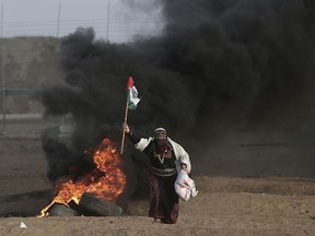 FILE - In this Oct. 5, 2018 file photo, a Palestinian woman wearing a traditional thobe, carries a Palestinian flag during a protest at the Gaza Strip's border with Israel. The thobe, a brightly embroidered robe for women, has long been a staple of Palestinian life, sewn by village women and worn at weddings and parties. Now it's gaining prominence as a softer symbol of Palestinian nationalism, competing with the classic keffiyeh. Rashida Tlaib proudly wore her thobe to her historic swearing-in as the first Palestinian American member of Congress, inspiring women around the world to tweet photos of themselves in their ancestral robes.